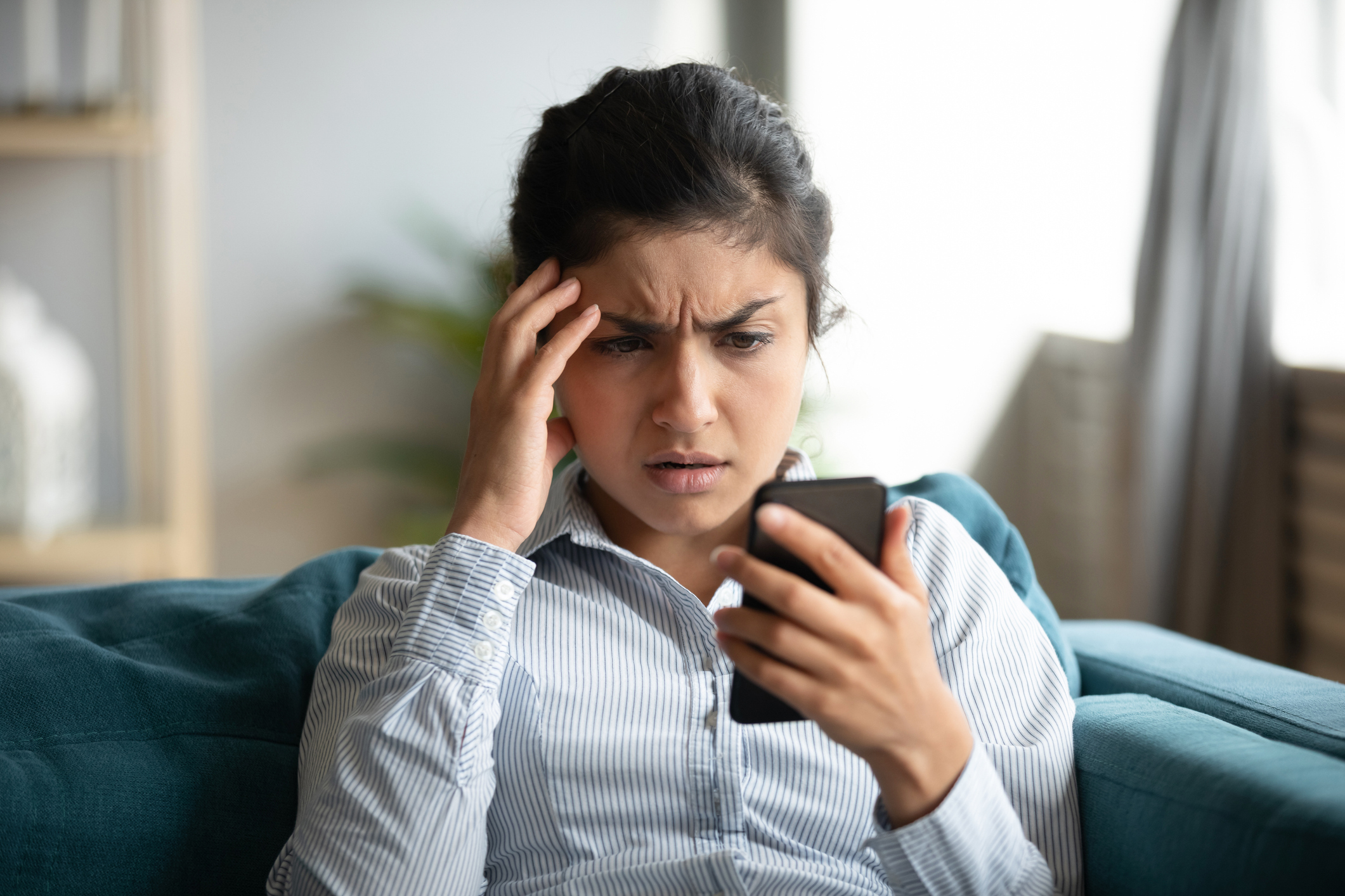 Concerned woman looking at cell phone as she sits on a couch.