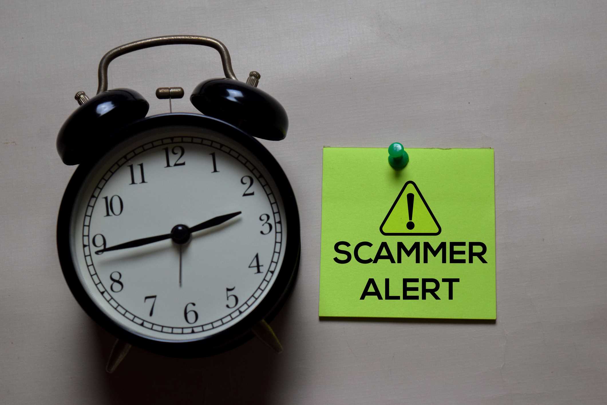 Scammer alert note tacked on wall next to a black alarm clock.