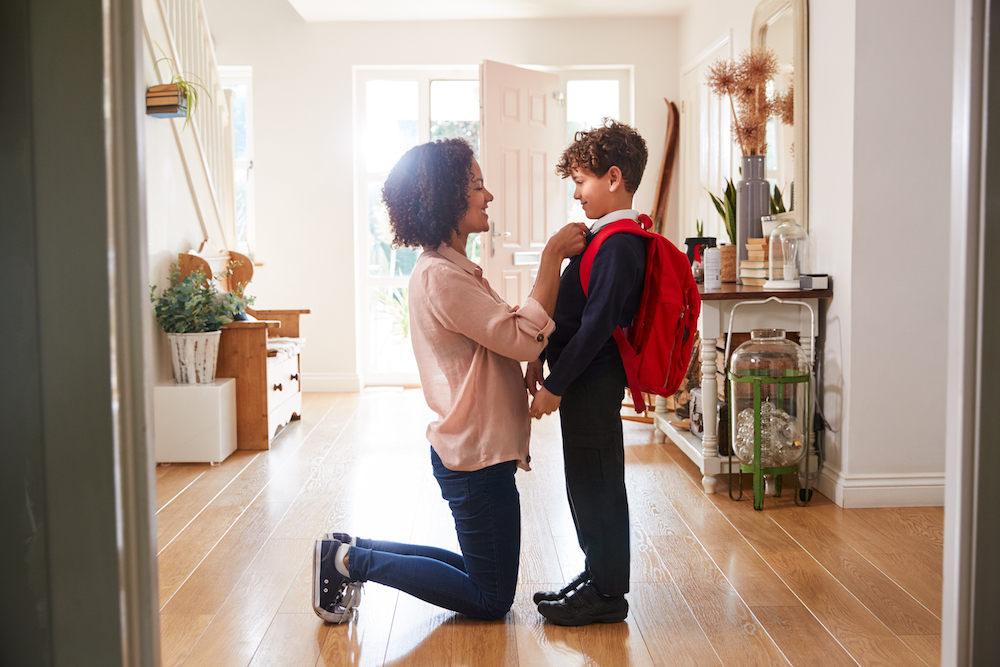 A woman kneeling down and getting a young boy ready to leave for school
