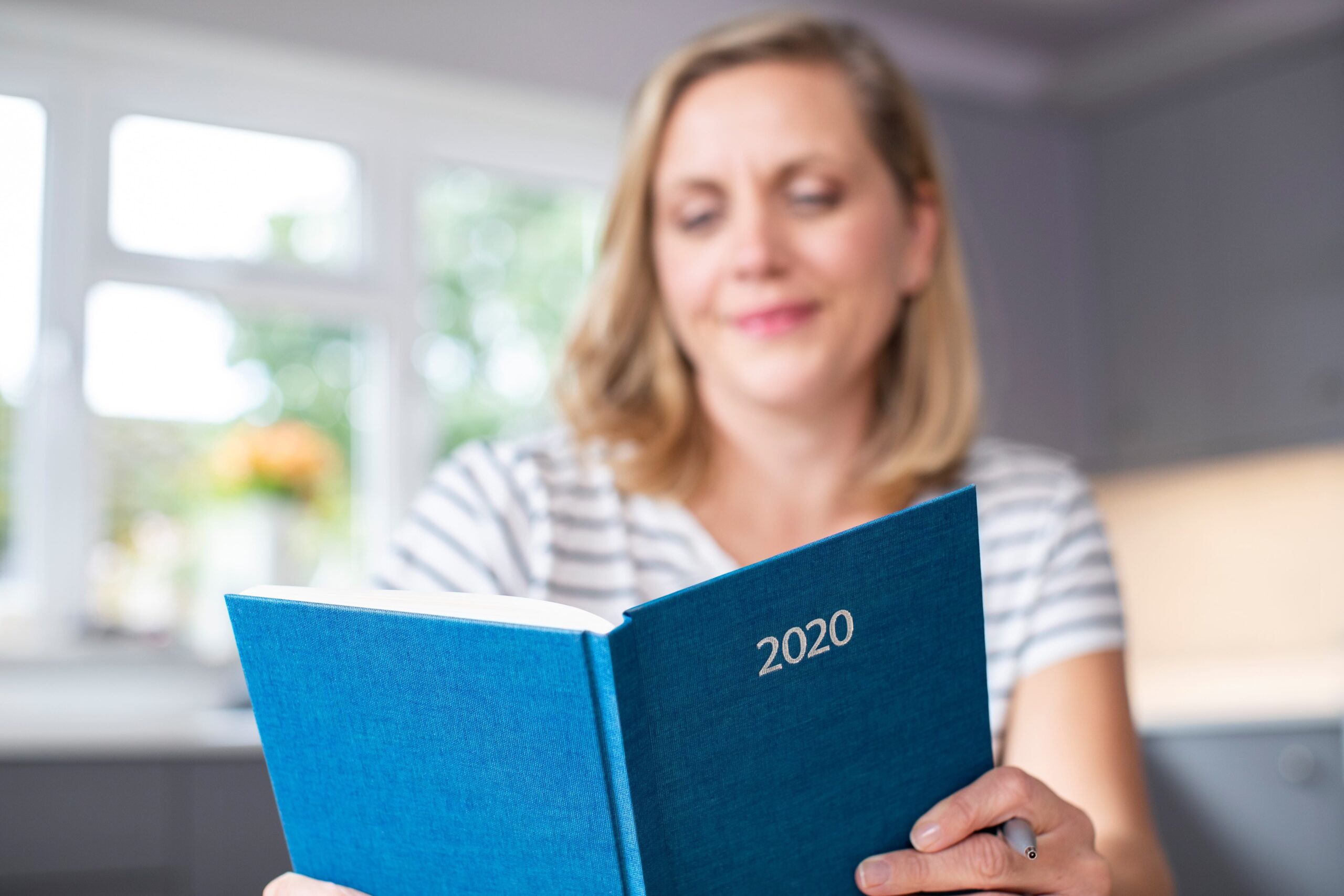 Woman reading resolutions in a bound journal with 2020 written on the cover.