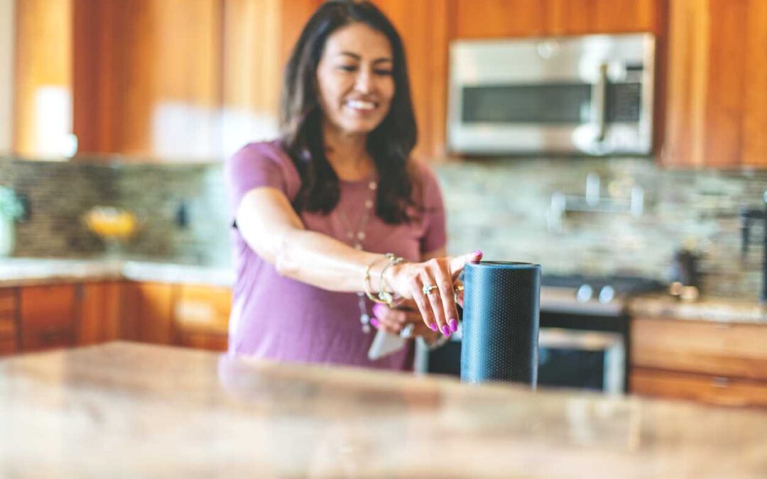 A woman standing in a home kitchen touches a smart speaker and practicing security for smart home.