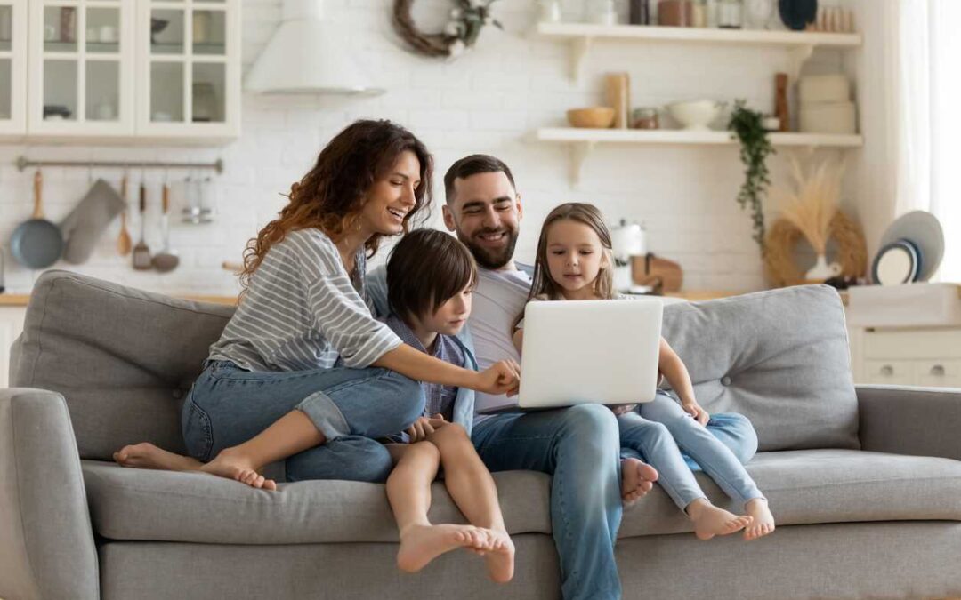 Mother, father, boy and girl sit on a sofa while looking at a laptop screen.