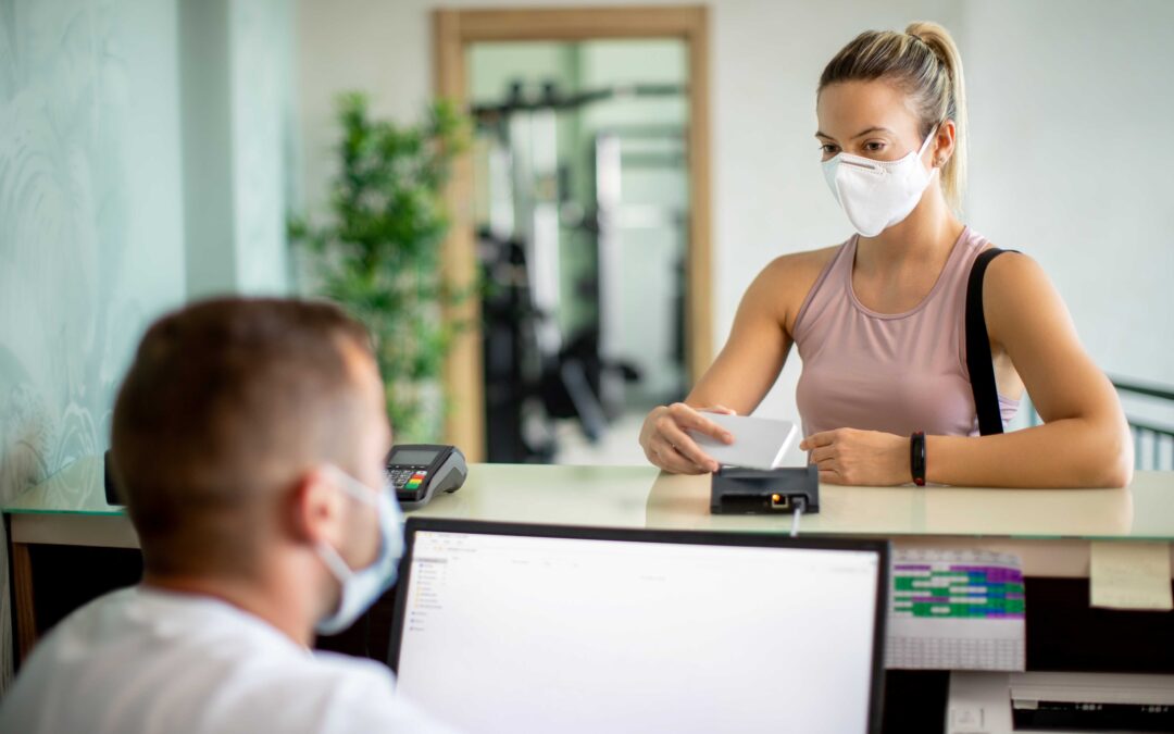 A woman wearing a white mask pays a bill at the gym using a mobile phone scanner.