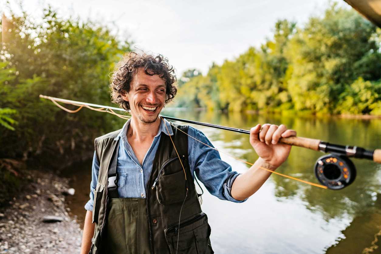 Smiling man holding a fishing pole next to a river.