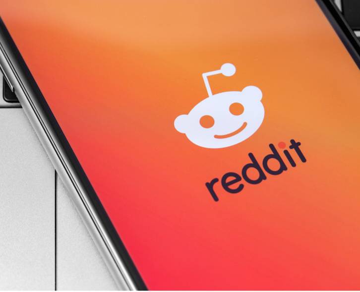 A smartphone laying on a computer keyboard with the Reddit app on the screen.