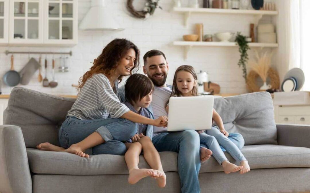 Mother, father, young boy and young girl, sitting on a sofa and preventing child identity theft using their laptop.